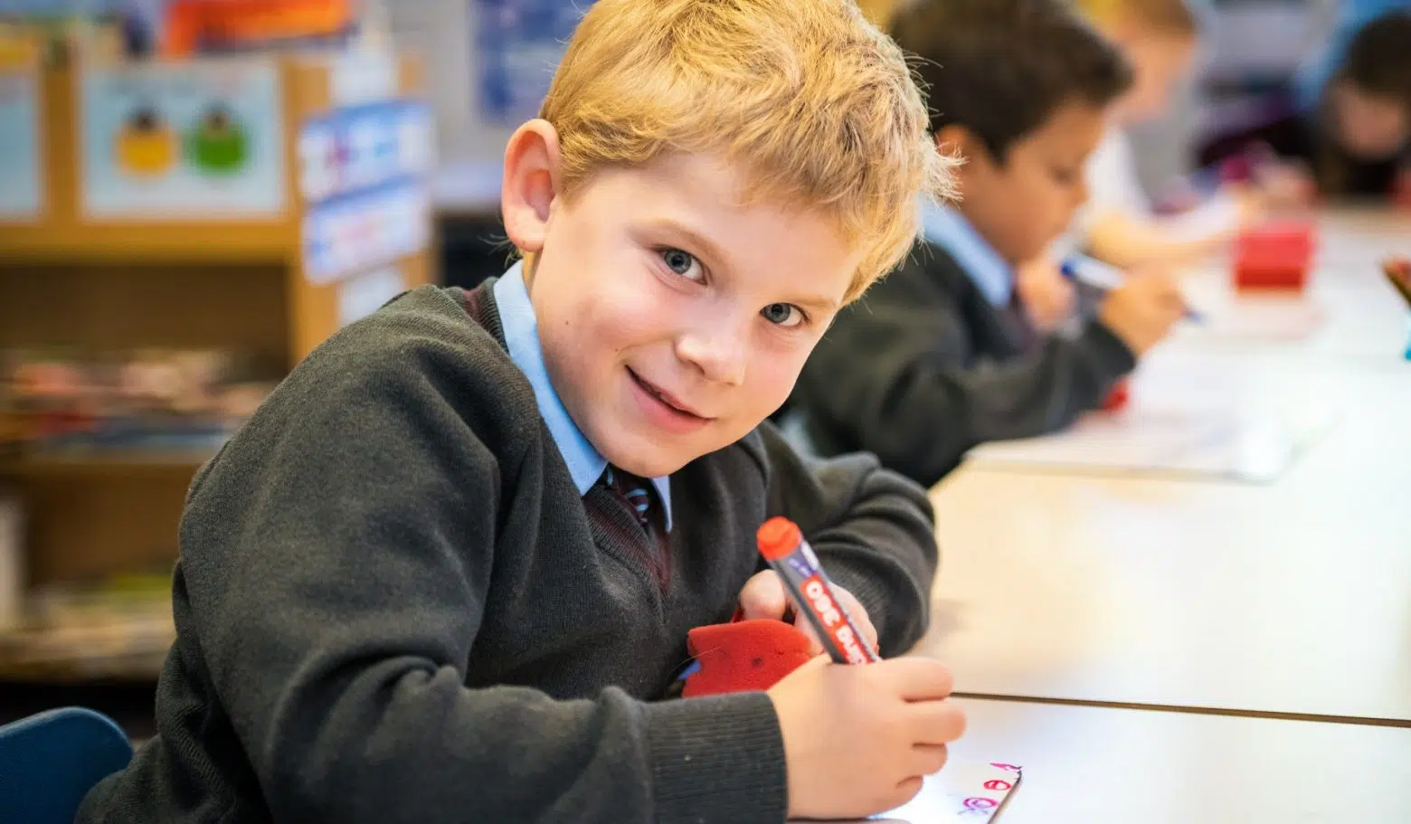 Smiling, young student writing on a whiteboard.